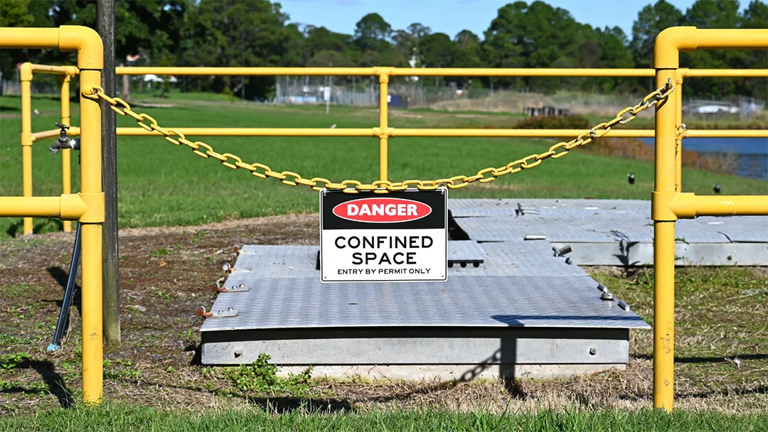 Yellow safety barriers frame confined space caution signage at work site